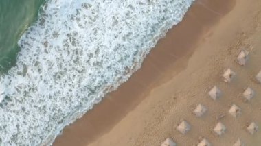 Pahalı deniz dalgaları, Karadeniz kıyısı, Bulgaristan yakınlarındaki saman güneşlikleri ve güneşlikleriyle boş ve güzel kumlu bir plajın üzerindeki video.