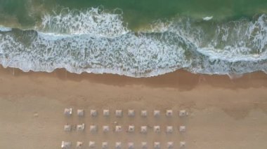 Pahalı deniz dalgaları, Karadeniz kıyısı, Bulgaristan yakınlarındaki saman güneşlikleri ve güneşlikleriyle boş ve güzel kumlu bir plajın üzerindeki video.