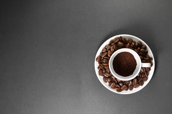 Une tasse avec des grains de café torréfiés fraîchement moulus avec des fruits de la plante de café avec une assiette . — Photo