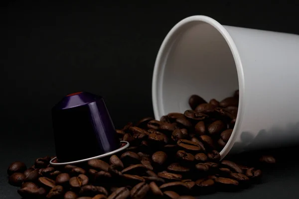 Plastic cup of white coffee lying, across a black background, with brown coffee beans inside the glass. Cafeteria and food. — Stock Photo, Image