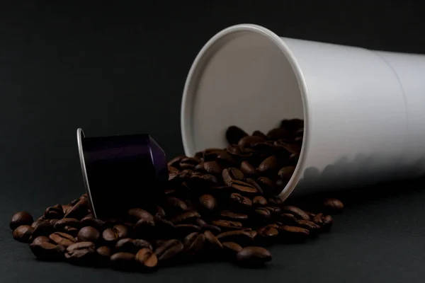 Plastikowa filiżanka białej kawy leżącej, na czarnym tle, z brązowymi ziaren kawy wewnątrz szkła. Kawiarnia i jedzenie. — Zdjęcie stockowe