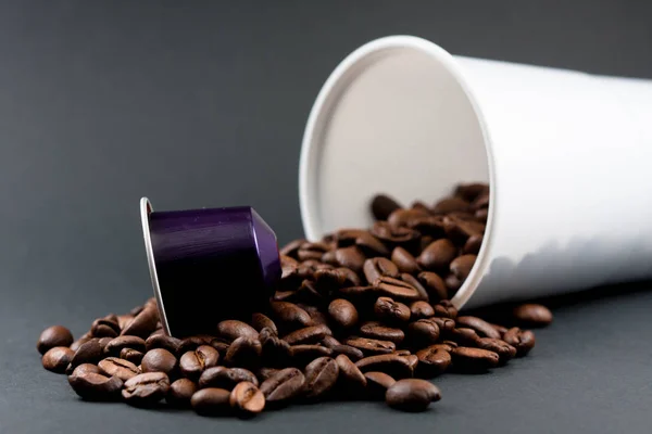 Plastic cup of white coffee lying, across a black background, with brown coffee beans inside the glass. Cafeteria and food.