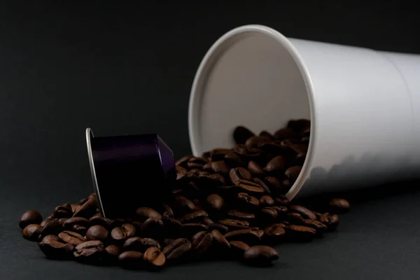 Tazza di plastica di caffè bianco sdraiato, su uno sfondo nero, con chicchi di caffè marrone all'interno del bicchiere. Caffetteria e cibo . — Foto Stock