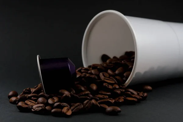 Plastic cup of white coffee lying, across a black background, with brown coffee beans inside the glass. Cafeteria and food.