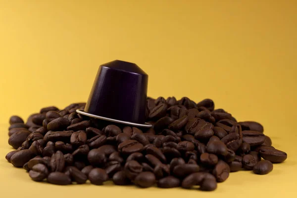 Layered coffee capsule, across a yellow background, with brown coffee beans under it. Coffee shop and food.