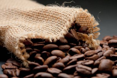 Açık sarı saman çuvalı, çuvalın içinde kahve çekirdekleri var. Siyah arka planda.