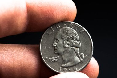 Adamın elinde gümüş bir Amerikan sikkesi var, çeyrek dolarlık sikkenin yakın çekimi siyahın üzerine izole edilmiş. Çanta, dolar.