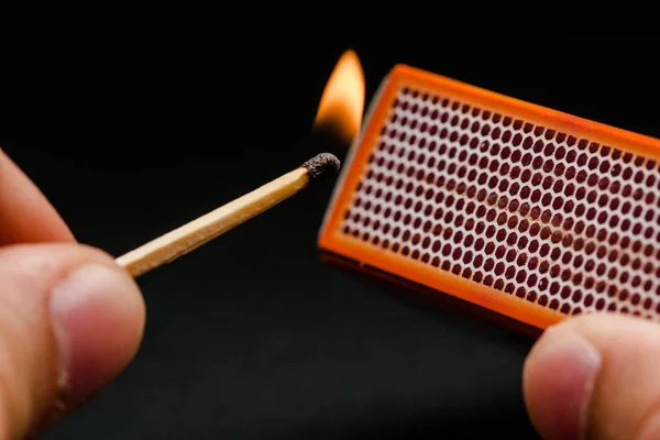 Man's fingers lighting a match, setting fire on friction. On a black background. Matches and fire. Smoke.