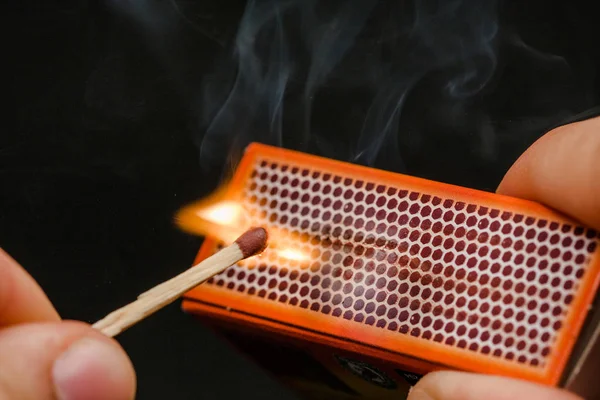 Man's fingers lighting a match, setting fire on friction. On a black background. Matches and fire. Smoke.