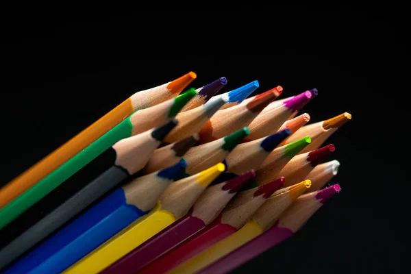 Houten potloden in alle kleuren gezien vanaf het blad van potloden. Gekleurde potloden gestapeld met een zwarte achtergrond. Kleuren. Terug naar school, onderwijs. — Stockfoto