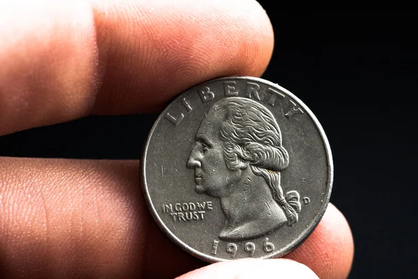 Adamın elinde gümüş bir Amerikan sikkesi var, çeyrek dolarlık sikkenin yakın çekimi siyahın üzerine izole edilmiş. Çanta, dolar.
