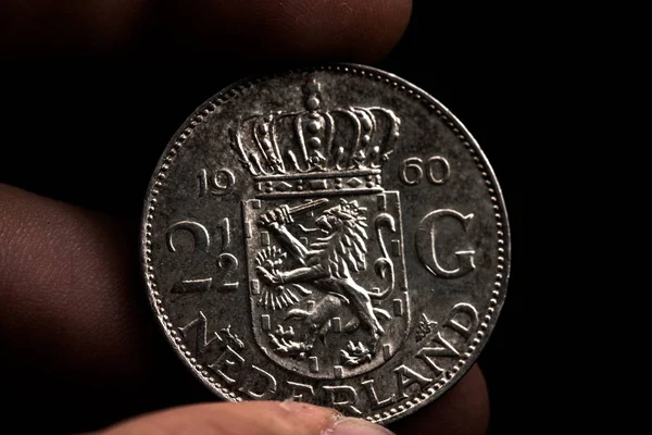 Mano de hombre sosteniendo una moneda holandesa. Del año 1960. De 2 florines y medio. Aislado sobre negro. Monedas . — Foto de Stock