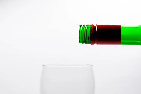 Glas mit Rotwein füllen, aus grüner Flasche eine grüne Flasche. auf weißem Hintergrund. — Stockfoto