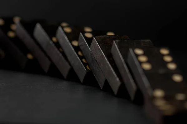 Domino etkisi, siyah domino taşları düşüyor, siyah bir arka plan üzerine. Domino oyunu.