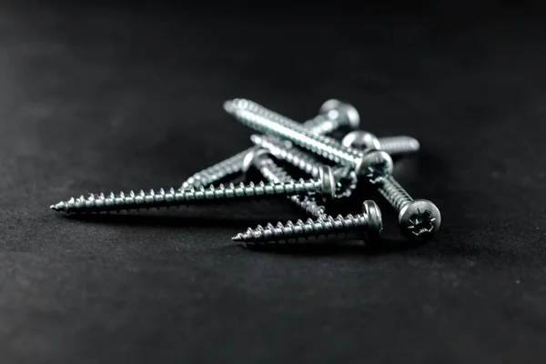 Steel screws grouped on a black background. Tools for DIY. — Stock Photo, Image