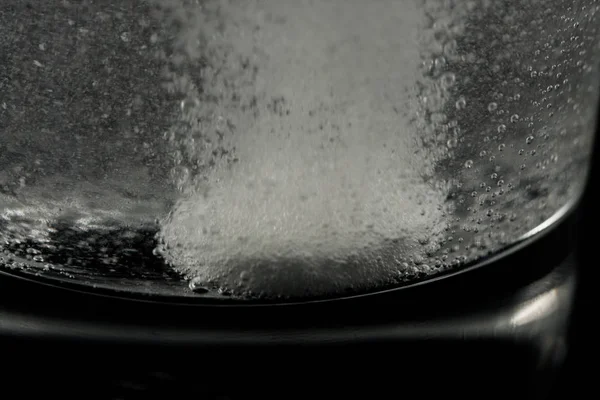 白色药片溶解在装满水的玻璃杯中。在黑色背景上行动. — 图库照片