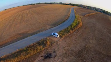 4k Bir toprak alanın ortasında bir yol boyunca çalışan beyaz bir aracın hava kaydı. Arka planda bazı binalar, güneşli mavi gökyüzü ile. Sevilla.