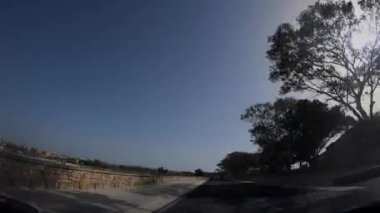 Birinci şahıs bakış açısı, bakış açısı, iç araç, ön camın arkasında, Malta'yı uçtan uca geçen kaputun perspektifi. Mavi bir gökyüzünde trafikte sürüş