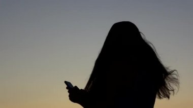 4k. Ultra Hd. Siluet dramatik günbatımı gökyüzü arka plan ile telefon kullanarak genç kadın. Her zaman bağlı, Internet teknolojisi kavramı.