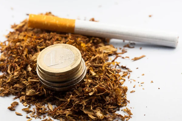 Τεμαχισμένο καπνό με κέρματα ευρώ γύρω, απομονωμένο σε λευκό φόντο. Ο καπνός μπορεί να προκαλέσει ασθένειες στον οργανισμό. — Φωτογραφία Αρχείου
