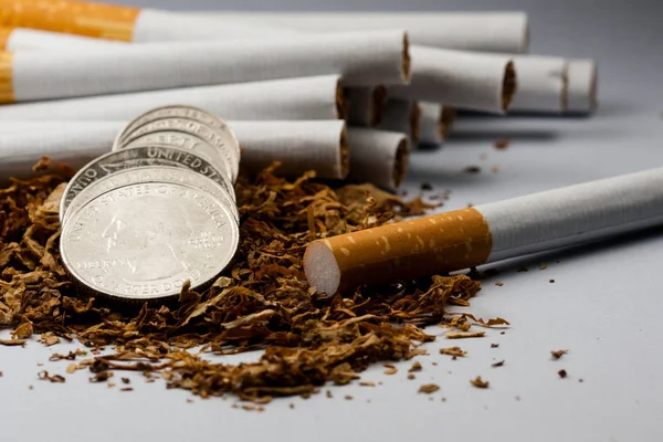 Τα τσιγάρα χωρίζονται με μερικά κομμάτια καπνού σκορπισμένα, με κέρματα σε δεκάρες γύρω, απομονωμένα σε λευκό φόντο. Ο καπνός μπορεί να προκαλέσει ασθένειες στον οργανισμό. — Φωτογραφία Αρχείου