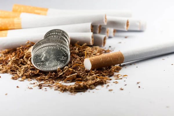 Сигарети розділені з розкиданим тютюном, з монетами в копійки навколо, ізольовані на білому тлі. Тютюн може спричинити захворювання в організмі. Це болить людське тіло . — стокове фото