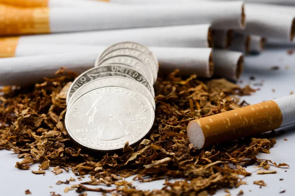 Сигарети розділені з розкиданим тютюном, з монетами в копійки навколо, ізольовані на білому тлі. Тютюн може спричинити захворювання в організмі . — стокове фото
