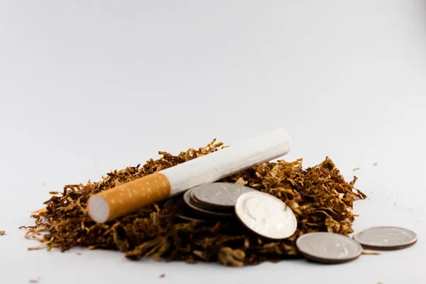 Cigarros separados com algum tabaco desfiado espalhado, com moedas em centavos ao redor, isolado em fundo branco. O tabaco pode causar doenças no organismo . — Fotografia de Stock