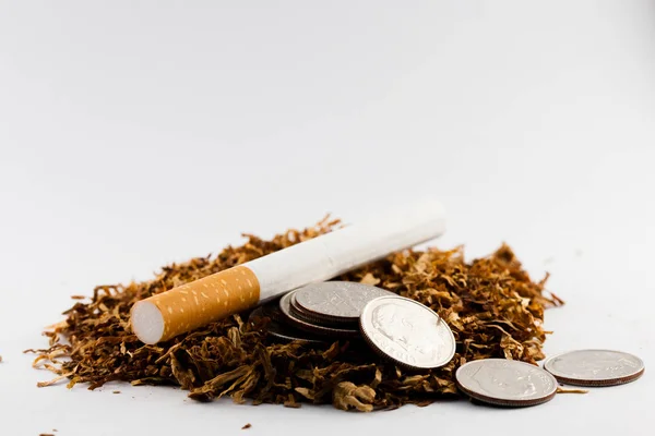 Cigarrillos separados con tabaco desmenuzado esparcido, con monedas en centavos alrededor, aisladas sobre fondo blanco. El tabaco puede causar enfermedades en el organismo . —  Fotos de Stock