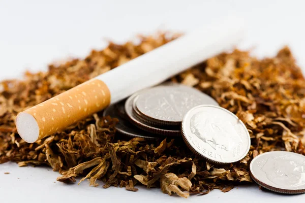 Cigarros separados com algum tabaco desfiado espalhado, com moedas em centavos ao redor, isolado em fundo branco. O tabaco pode causar doenças no organismo . — Fotografia de Stock