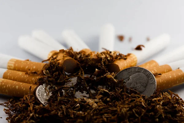 Cigarros separados com algum tabaco desfiado espalhado, com moedas em centavos ao redor, isolado em fundo branco. O tabaco pode causar doenças no organismo . — Fotografia de Stock