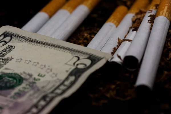 Сигарети розділені з розкиданим тютюном, з монетами в копійки навколо і деякими доларами, ізольовані на білому тлі. Тютюн може спричинити захворювання . — стокове фото