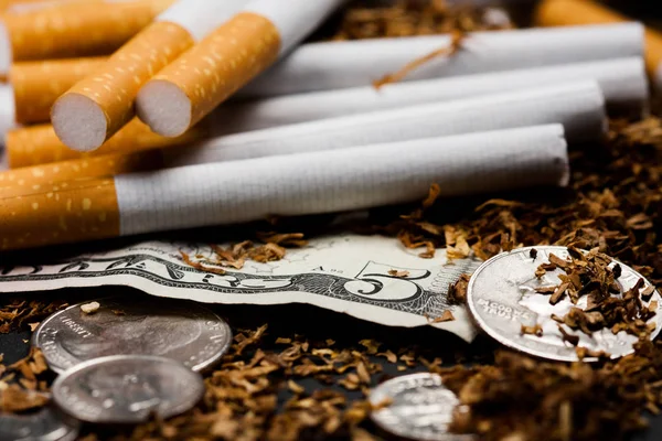 Τα τσιγάρα χωρίζονται με λίγο καπνό σκορπισμένο, με δεκάρες γύρω και μερικά δολάρια, απομονωμένα σε μαύρο φόντο. Ο καπνός μπορεί να προκαλέσει ασθένειες. — Φωτογραφία Αρχείου