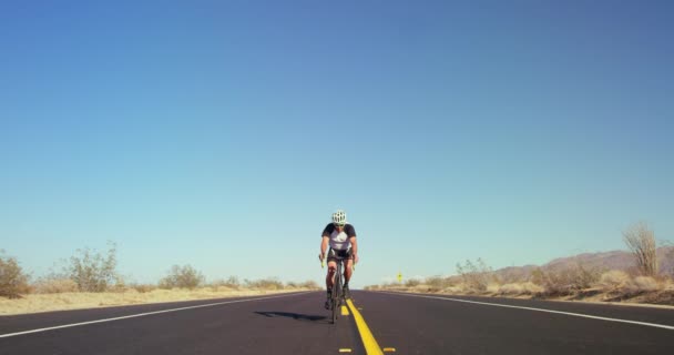 背景の青空と晴れた日に外の砂漠の道をロードバイクでサイクリング スローモーション若い健康な男 — ストック動画