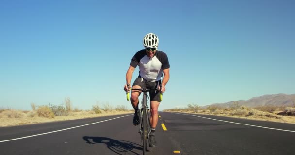慢动作年轻健康的人骑自行车在沙漠路外面在阳光明媚的天 背景蓝色的天空的道路自行车 — 图库视频影像