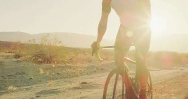 慢动作年轻男子骑自行车自行车在沙漠公路外的日落与镜头耀斑 — 图库视频影像