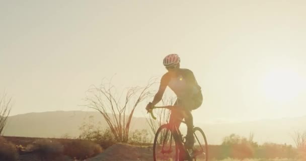 年轻健康活跃男子骑自行车在沙漠公路外的道路自行车日落与透镜耀斑 — 图库视频影像
