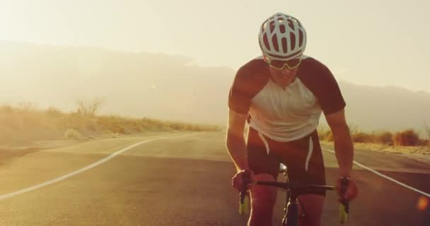 夕暮れレンズ フレアの外の砂漠の道をロードバイクでサイクリング健康的なアクティブな若者 — ストック動画
