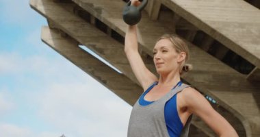 Taş köprü altında kettlebell ile egzersiz yaparak genç güçlü kadın