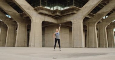 Taş köprü altında kettlebell ile egzersiz yaparak genç güçlü kadın