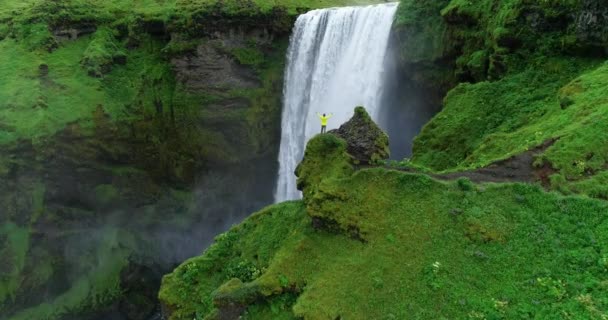 男は身に着けているアイスランドの山の中を流れる巨大な滝の黄色いレインコートを着て楽しんでビュー — ストック動画