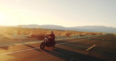 Genç sürme vintage siyah motosiklet çöl otoyol aşağı günbatımında adam.