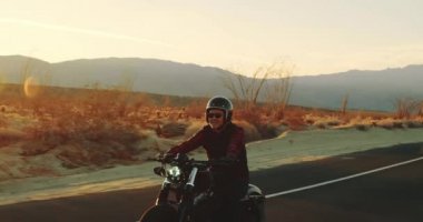 Genç sürme vintage siyah motosiklet çöl otoyol aşağı günbatımında adam.