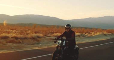 Genç sürme vintage siyah motosiklet çöl otoyol aşağı günbatımında adam.