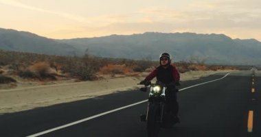 Genç sürme vintage siyah motosiklet çöl otoyol aşağı günbatımında adam.