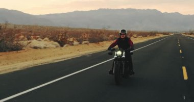 Genç sürme vintage siyah motosiklet çöl otoyol aşağı günbatımında adam.