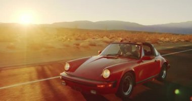 Mutlu çiftin Vintage Cabrio spor araba günbatımında ülke yolda sürüş havadan görünümü