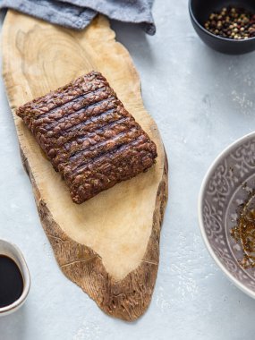 Grilled tempeh on a wooden board, soy sauce, spices, bright background. Vegan protein.