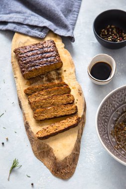 Slices of grilled tempeh on a wooden board, soy sauce, spices, bright background. Vegan protein.