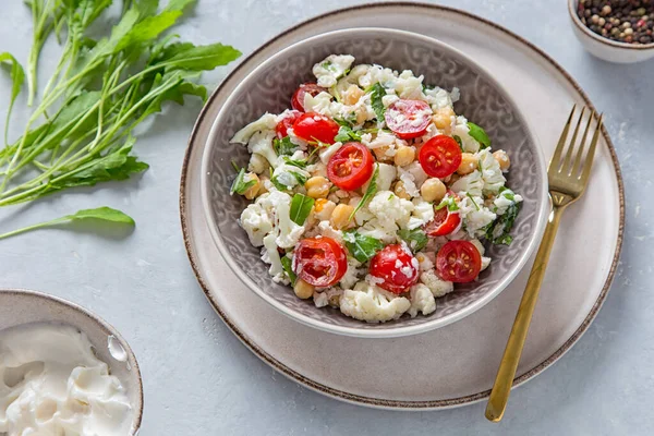 Raw cauliflower salad with chickpeas, tomatoes, arugula and mayonnaise, a complete vegan meal.